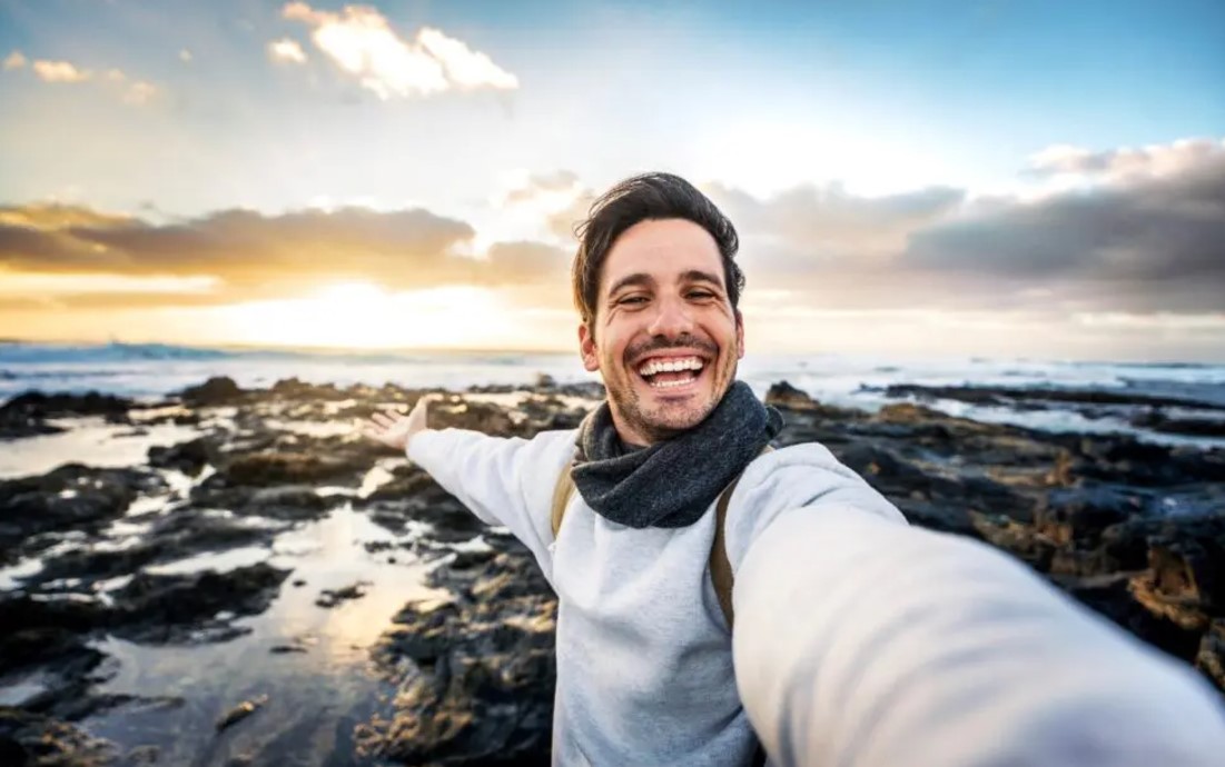 A smiling man taking a selfie in front of a body of water.