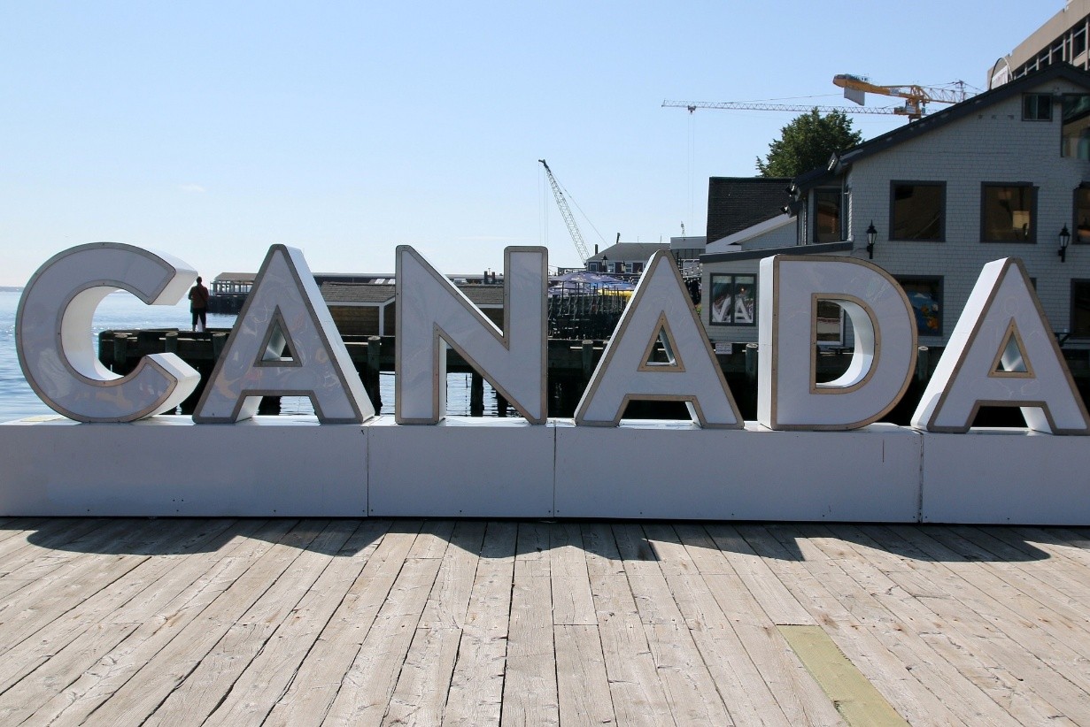 A large sign on a dock with people-sized letters that says “Canada” and a wharf in the background. 