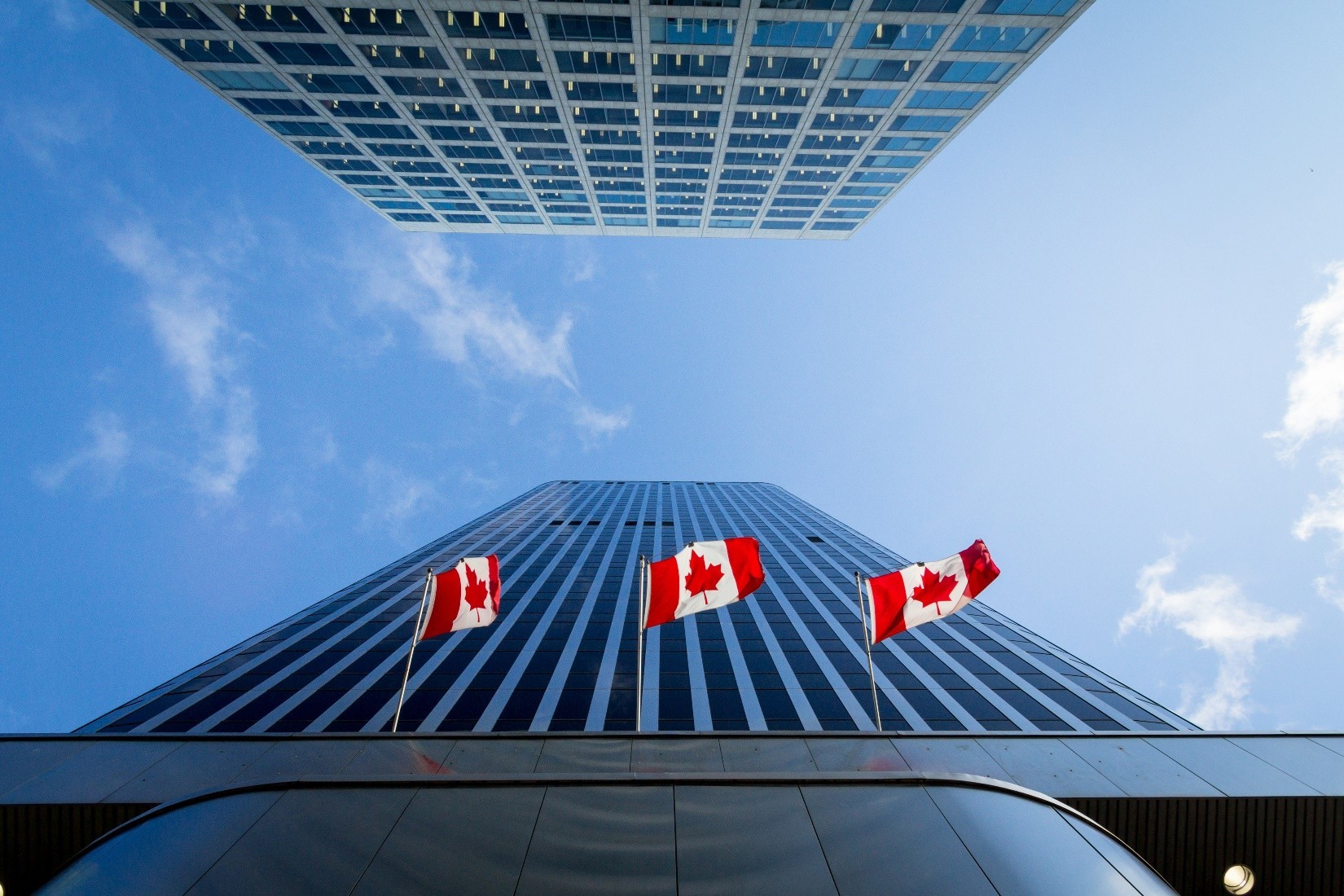 Three Canadian Flags flying outside a tall office building.