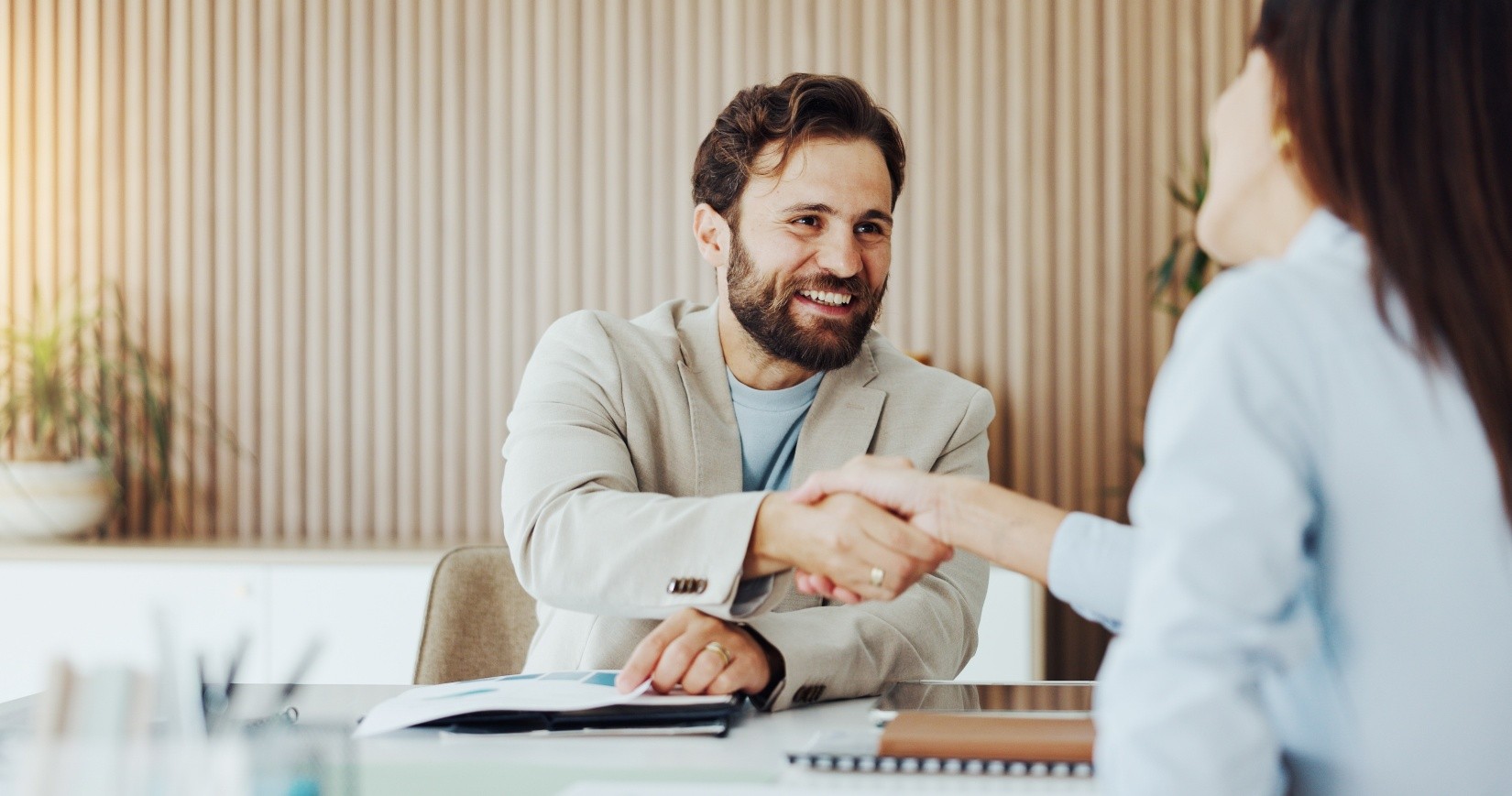 A man wearing a blazer shaking hands with a woman and smiling. 