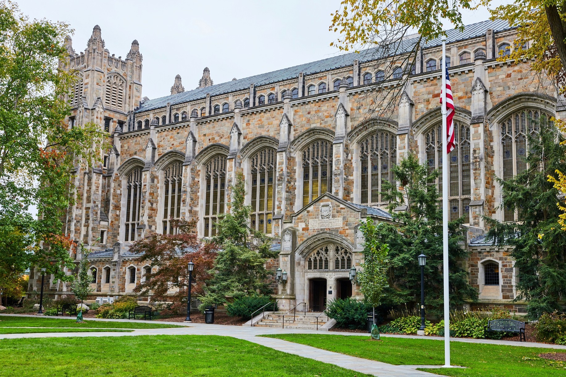 A gothic-style building on the University of Michigan campus with a flagpole with an American flag in front of it.