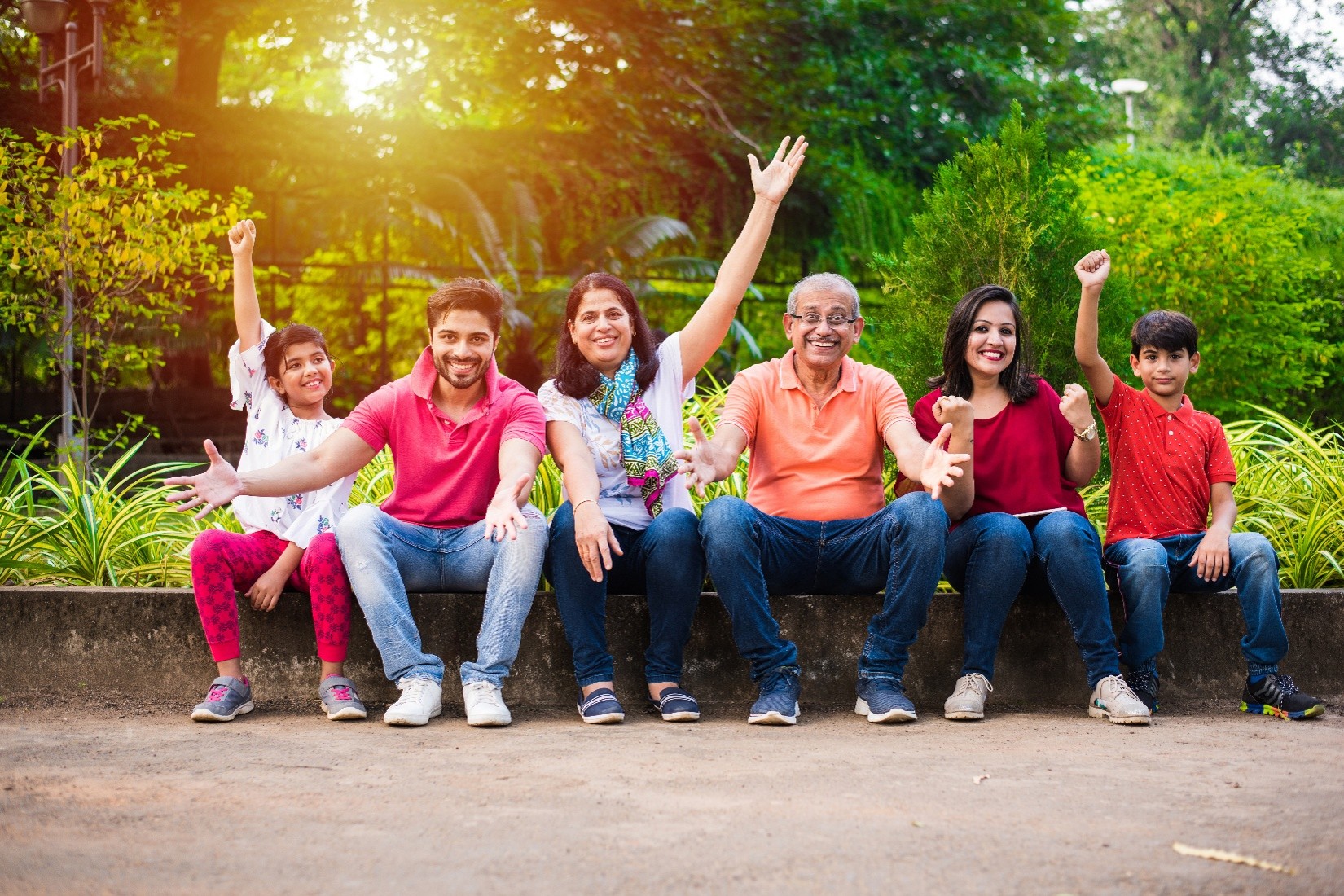 A family with multiple generations including grandparents, parents, and kids, sitting<br />
outside with their arms extended while smiling.   