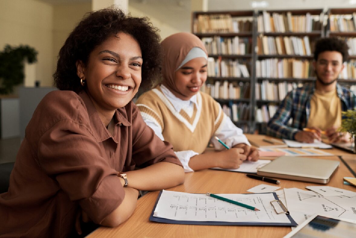 A smiling young woman sitting at a table, studying with two other young people as part<br />
of a Canadian work and study permit program.   