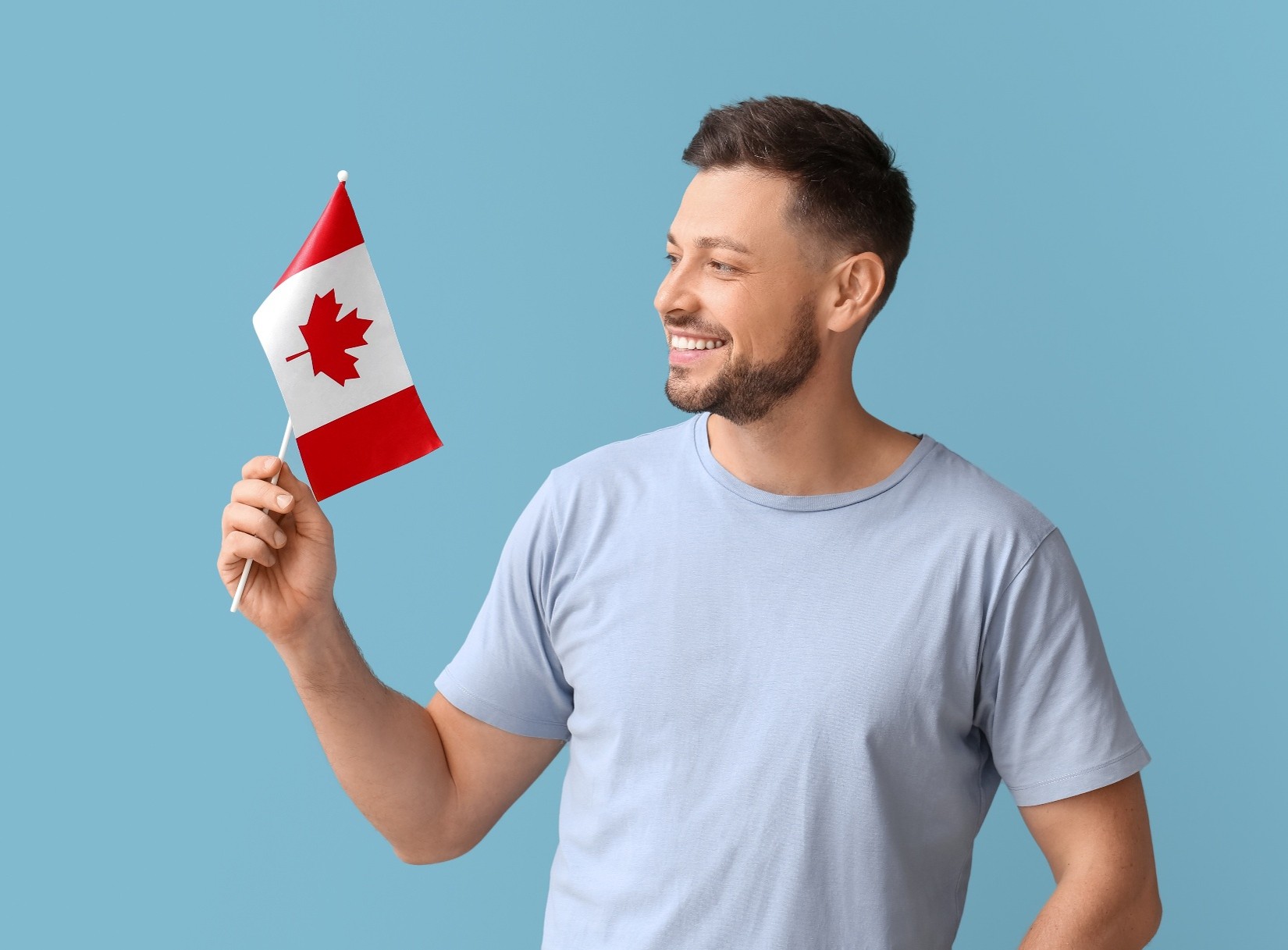 A man who has his successfully gotten his Canadian citizenship, holding a small<br />
Canadian flag and smiling at it.   