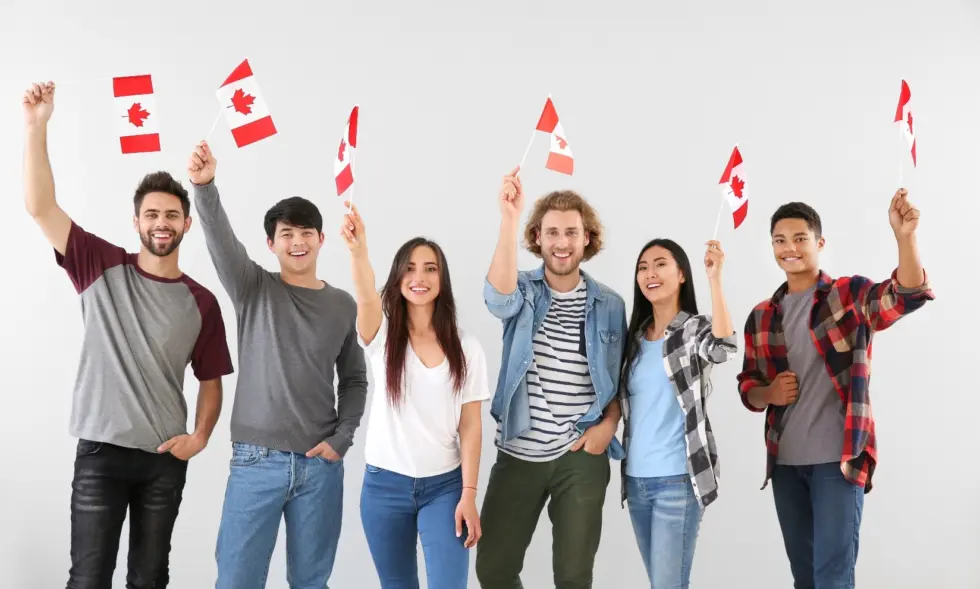 Six young men and women participating in work or study permits, standing together and holding up small Canadian flags<br />
