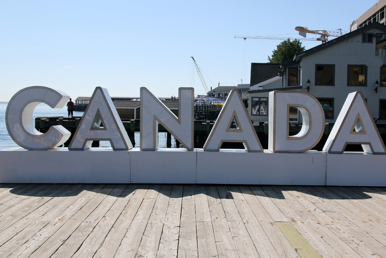 A large sign on a dock with people-sized letters that says “Canada” and a wharf in the background.