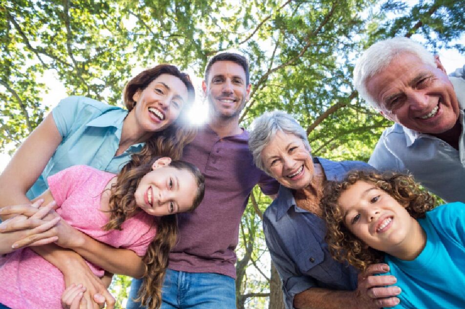 A smiling family of two children, their parents, and their grandparents pictured from<br />
below looking down at the ground with trees overhead.  
