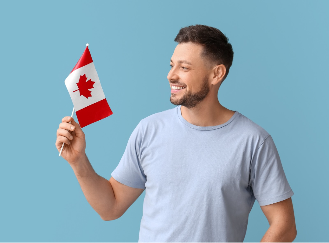 A man who has his successfully gotten his Canadian citizenship, holding a small Canadian flag and smiling at it.