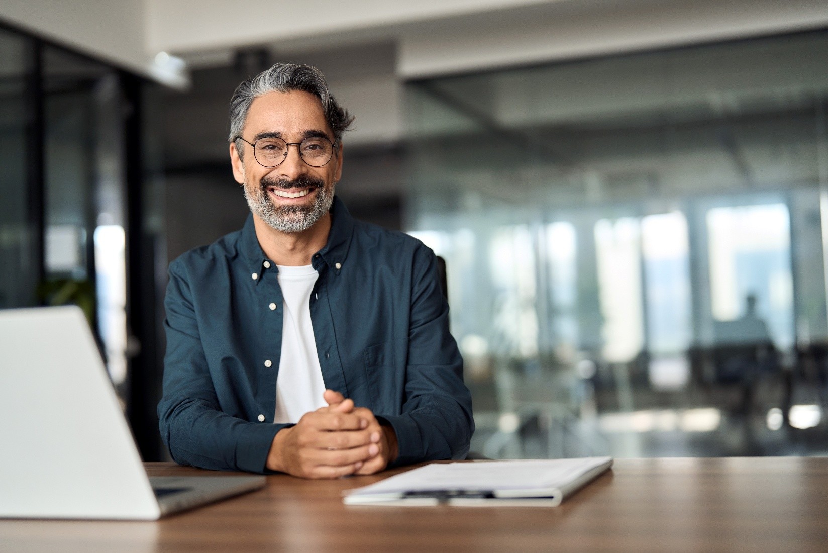 A wealthy man sitting at a desk wearing glasses and learning about the EB-5 Green Card<br />
investment. 