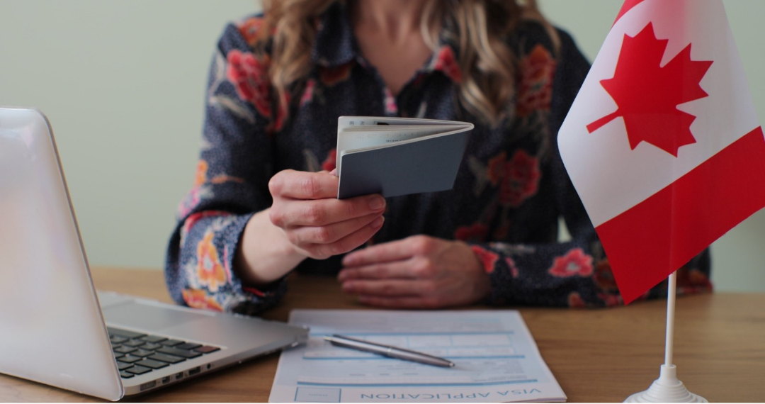 Person reviewing passport documents beside a Canadian flag while completing a Canadian citizenship or visa application process.