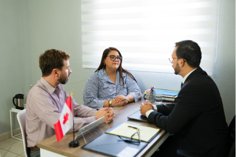 A person in a black blazer speaking to a couple with a Canada flag on the table
