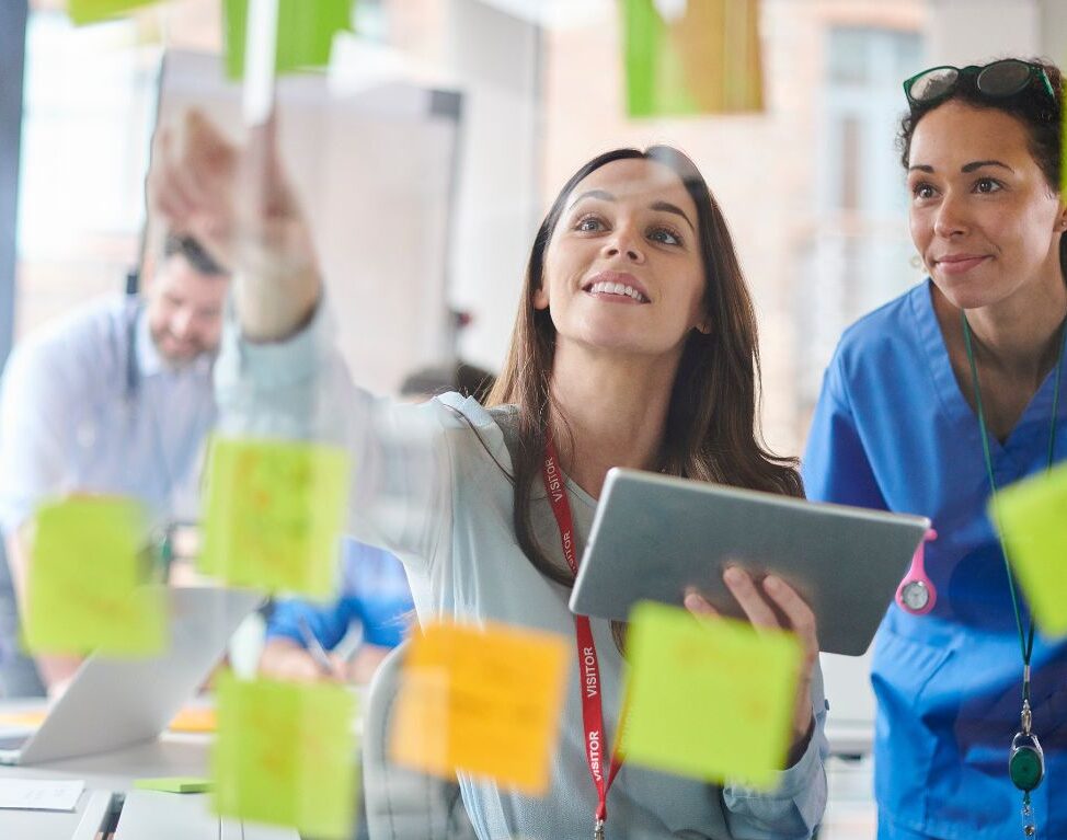 two people looking at a glass Kanban board with notes on it